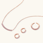 Rose gold pavé zirconia bar necklace, hoop earrings, and open ring set with pink stones on cream background.