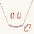 Rose gold pavé zirconia bar necklace, hoop earrings, and open ring set with pink stones on cream background.