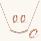 Rose gold pavé zirconia bar necklace, hoop earrings, and open ring set with pink stones on cream background.