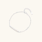Delicate rhodium-plated silver chain bracelet with row of small baroque pearls centered on white background.