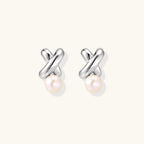 Rhodium-plated silver earrings with twisted X design and freshwater pearl drops on beige background