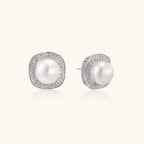 Rhodium-plated sterling silver stud earrings with round freshwater pearls surrounded by geometric crystal halos on cream background.