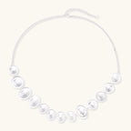 Graduated pearl-finish silver discs forming an organic bubble bib necklace on delicate chain against cream background.