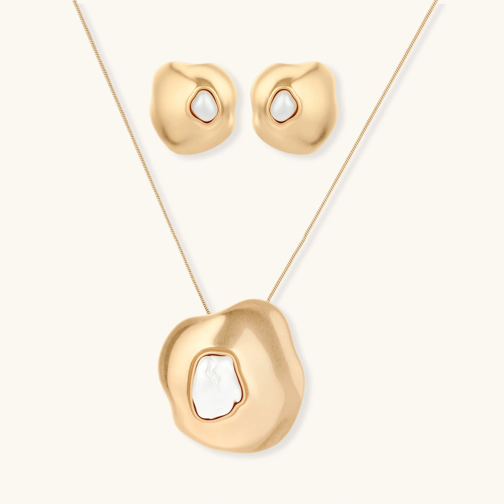 Close-up of organic gold-toned earrings and necklace with white baroque pearls on neutral background.