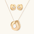 Close-up of organic gold-toned earrings and necklace with white baroque pearls on neutral background.