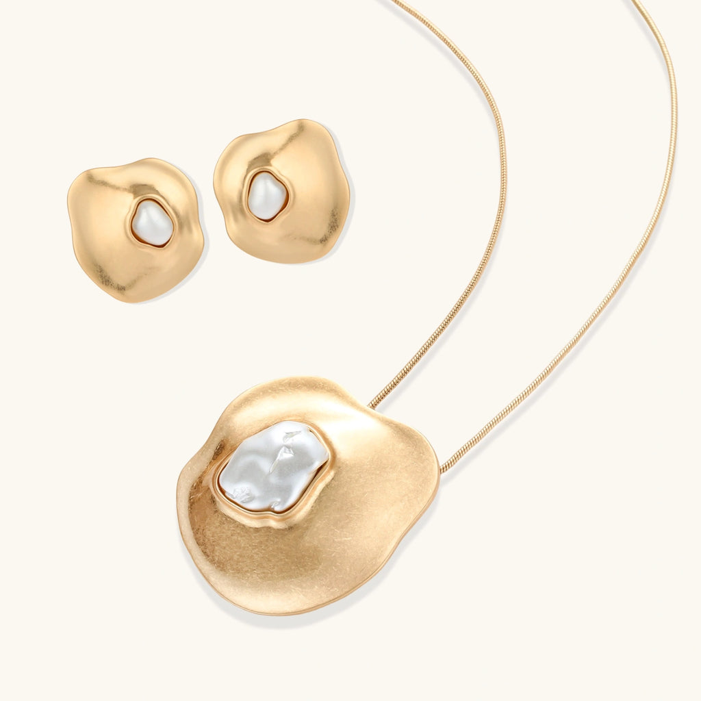 Close-up of organic gold-toned earrings and necklace with white baroque pearls on neutral background.