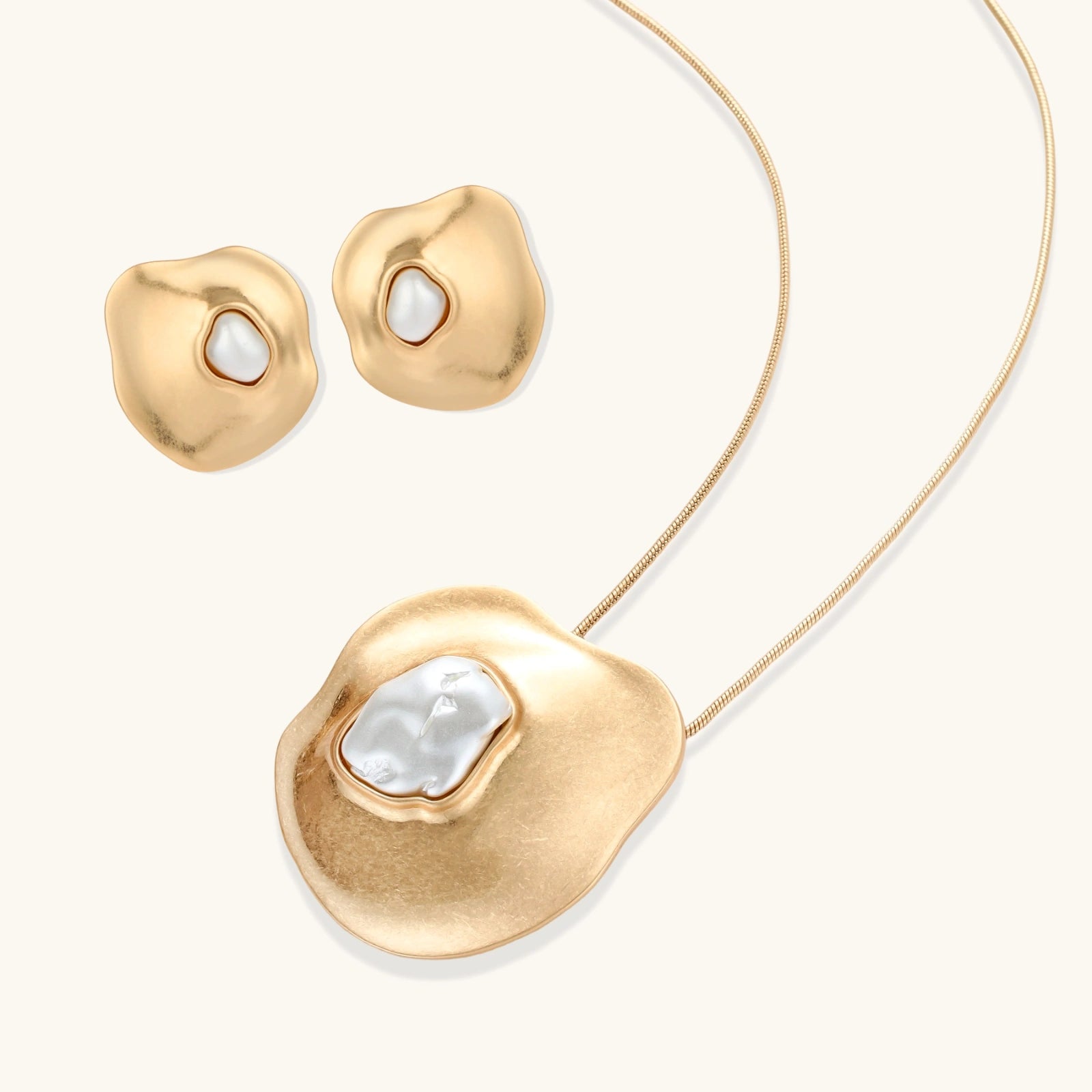 Close-up of organic gold-toned earrings and necklace with white baroque pearls on neutral background.