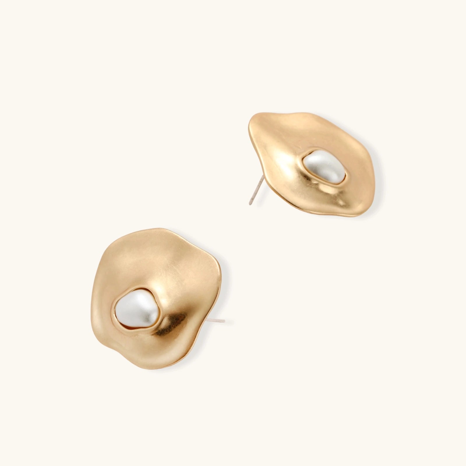 Close-up of organic gold-toned earrings and necklace with white baroque pearls on neutral background.