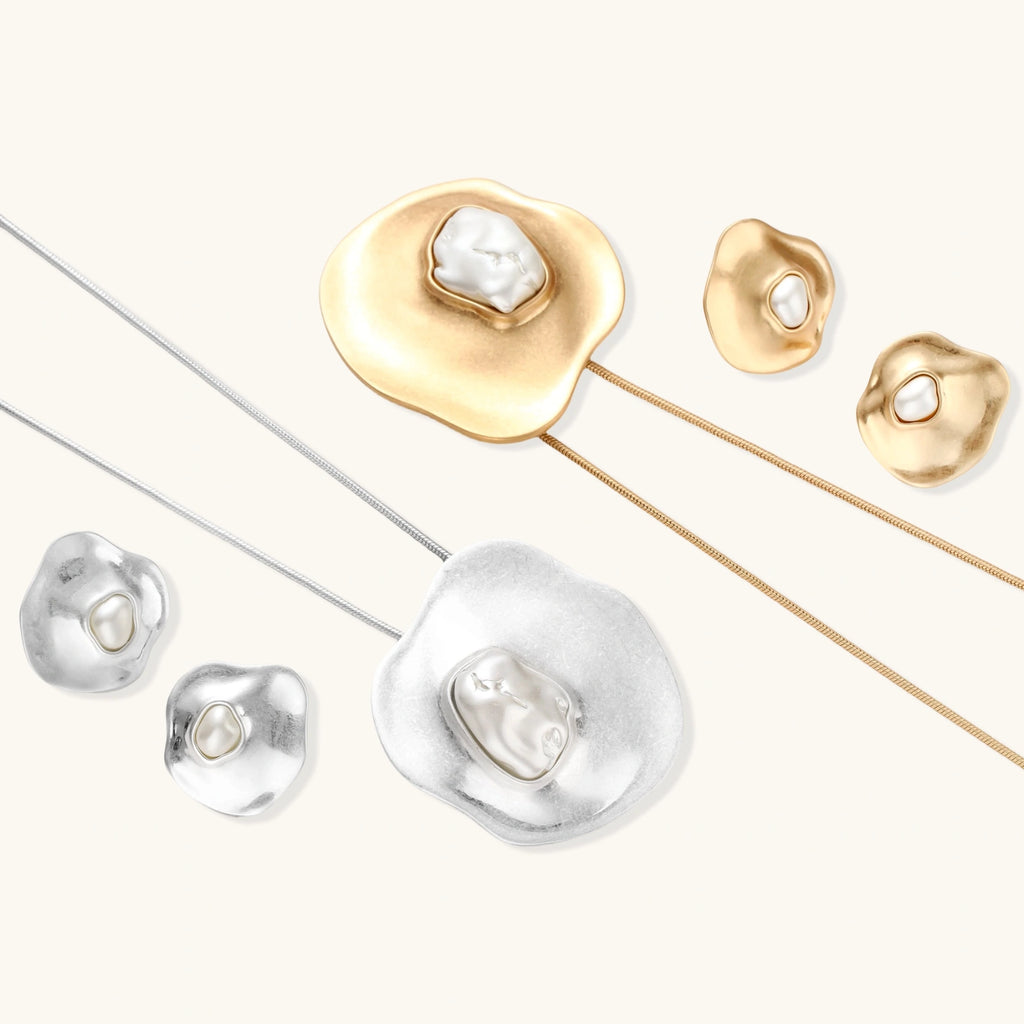 Close-up of organic gold-toned earrings and necklace with white baroque pearls on neutral background.
