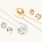 Close-up of organic gold-toned earrings and necklace with white baroque pearls on neutral background.