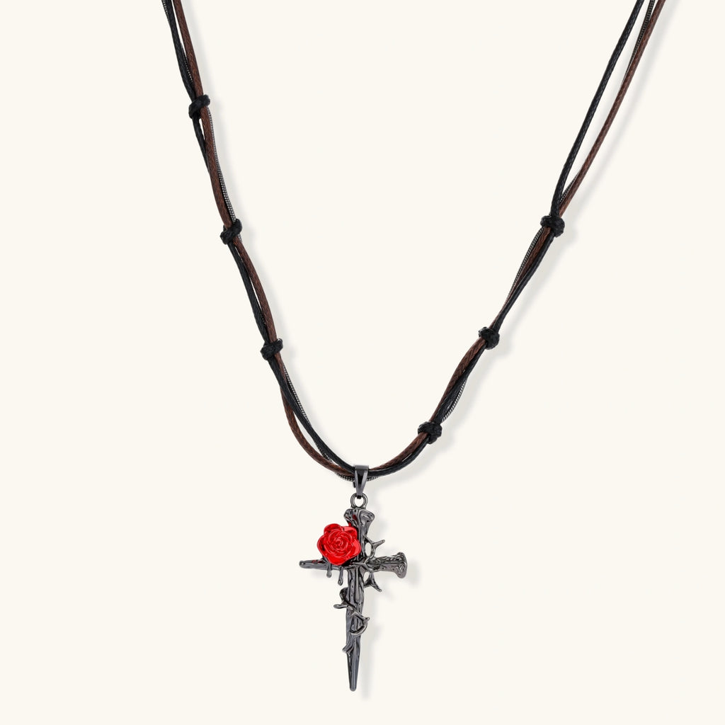 Gothic cross pendant with red enamel rose and thorn details on adjustable brown cord necklace against white background.