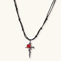 Gothic cross pendant with red enamel rose and thorn details on adjustable brown cord necklace against white background.