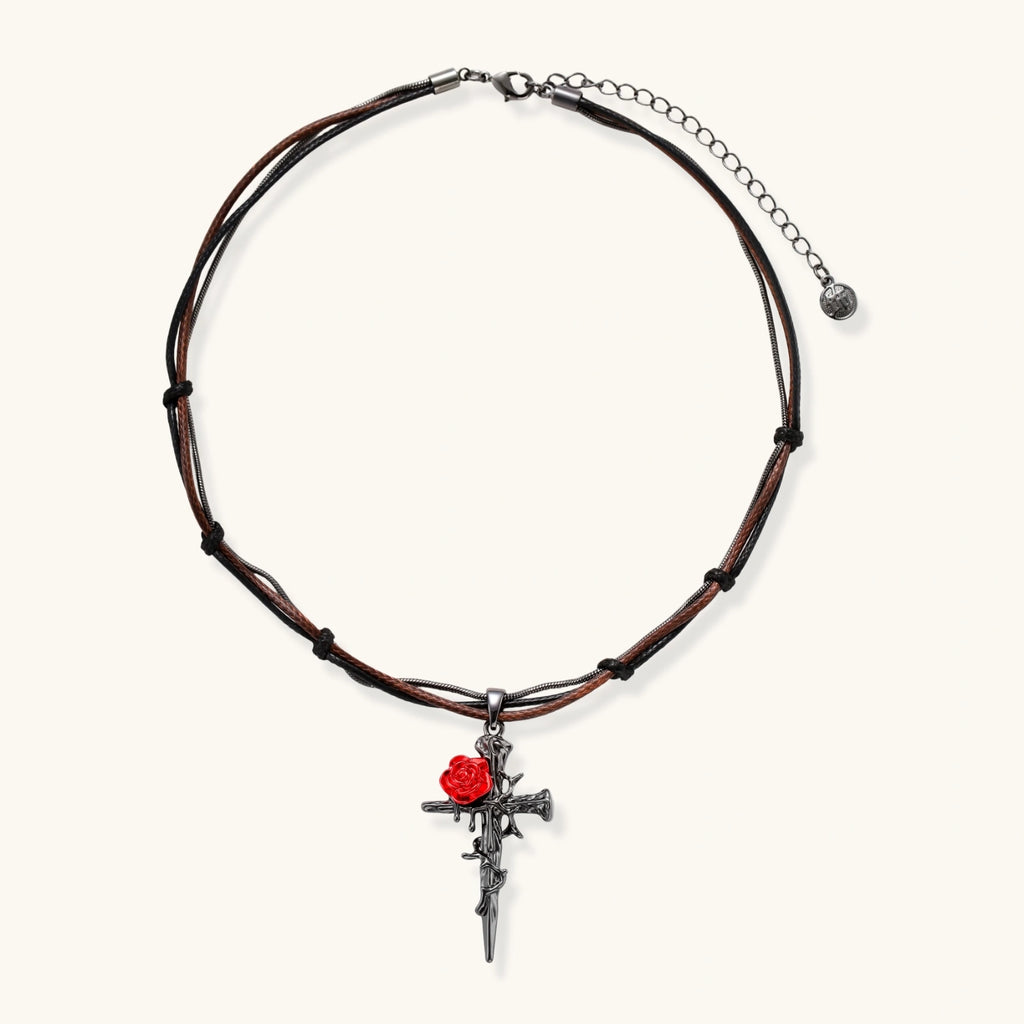 Gothic cross pendant with red enamel rose and thorn details on adjustable brown cord necklace against white background.
