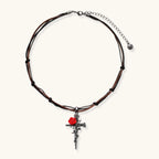Gothic cross pendant with red enamel rose and thorn details on adjustable brown cord necklace against white background.