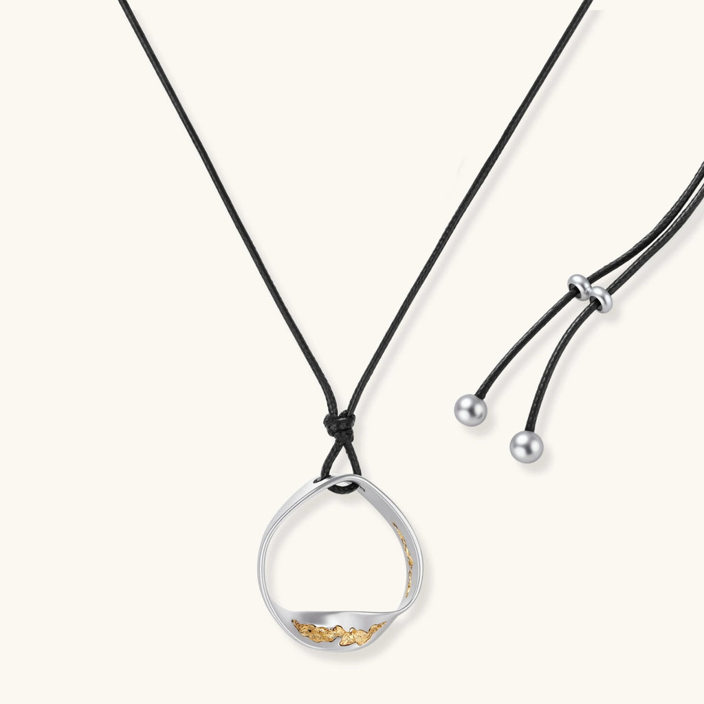 Artistic jewelry set featuring curved silver pendant with gold veining on black cord plus matching asymmetrical hoop earrings