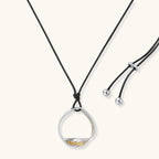 Artistic jewelry set featuring curved silver pendant with gold veining on black cord plus matching asymmetrical hoop earrings
