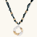 Adjustable necklace with black paisley fabric cord, gold metal spacers, and clear twisted pendant on cream background