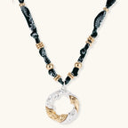Adjustable necklace with black paisley fabric cord, gold metal spacers, and clear twisted pendant on cream background