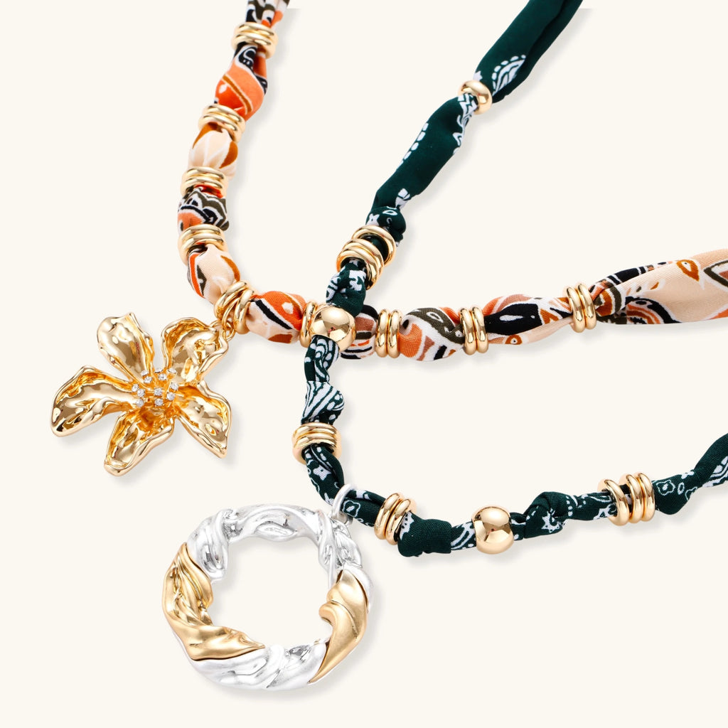 Adjustable necklace with black paisley fabric cord, gold metal spacers, and clear twisted pendant on cream background