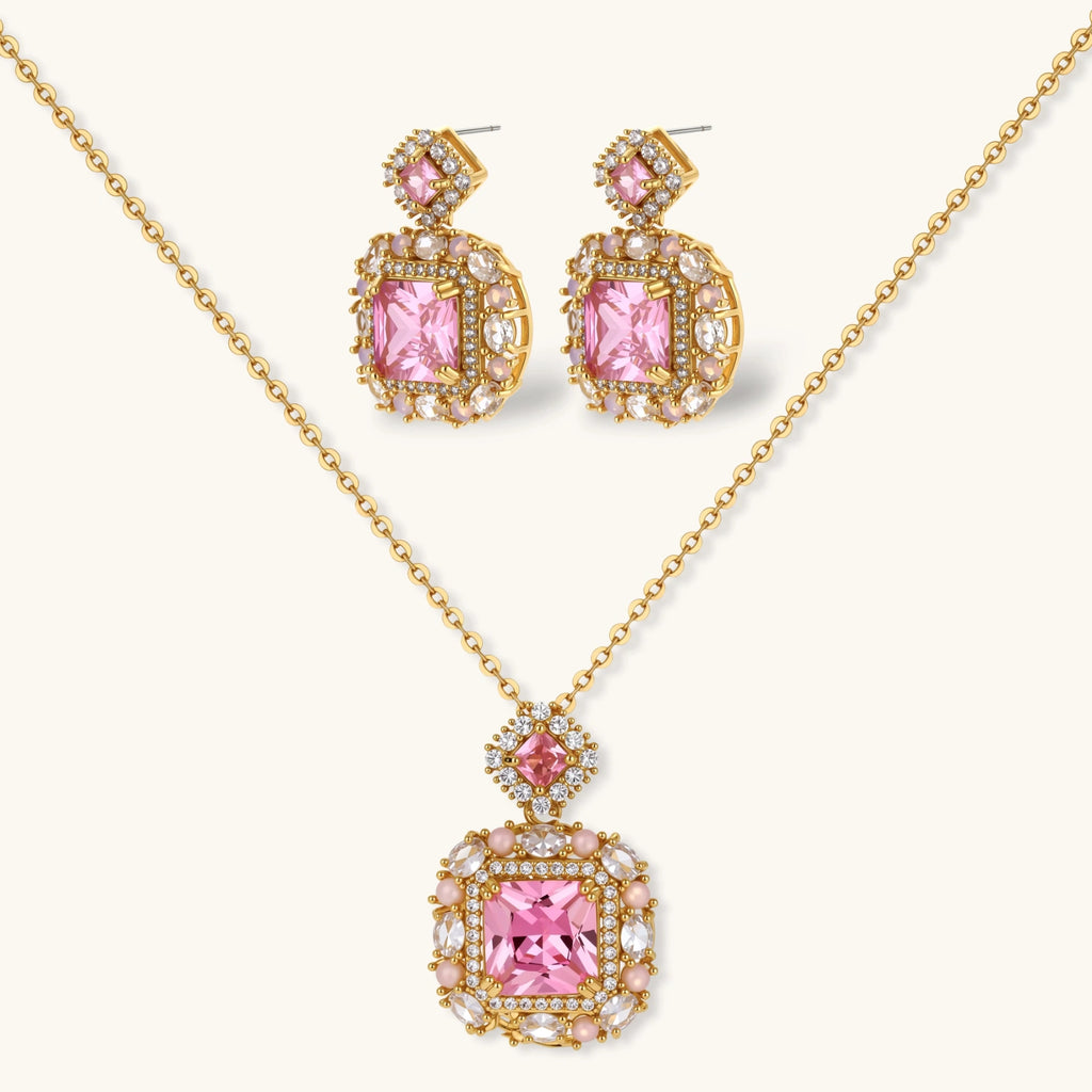 Ornate gold-plated jewelry set with rose pink zirconia center stones and crystal accents on cream background.