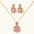 Ornate gold-plated jewelry set with rose pink zirconia center stones and crystal accents on cream background.