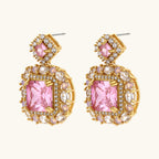 Ornate gold-plated jewelry set with rose pink zirconia center stones and crystal accents on cream background.